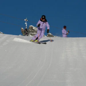 Skifahrer in lila Skiausrüstung auf perfekt präparierter Piste bei sonnigem Wetter.